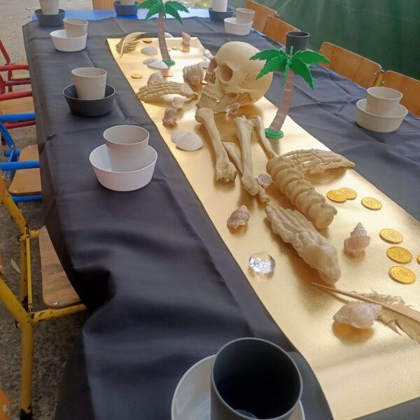 A pirate party table set up with black table cloth, skeletons, gold and plates