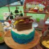 an image of a birthday cake with a treasure chest on top. The background is a childs pirate party