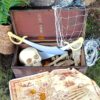 A wooden treasure chest sits open. There is a net, skull, swords and treasure inside. There is a treasure map in front of it.