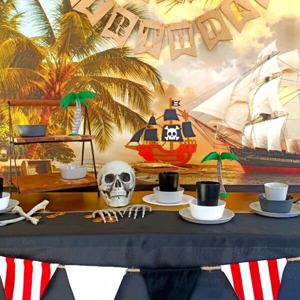 A pirate party table set up with black table cloth, skeletons, gold and plates