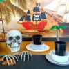 A pirate party table set up with black table cloth, skeletons, gold and plates