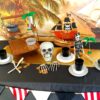A pirate party table set up with black table cloth, skeletons, gold and plates