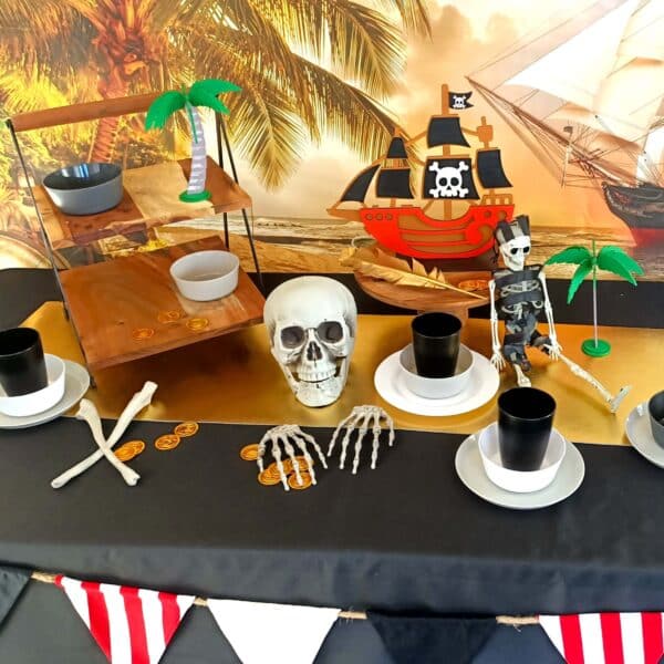 A pirate party table set up with black table cloth, skeletons, gold and plates