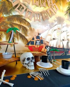 A pirate party table set up with black table cloth, skeletons, gold and plates