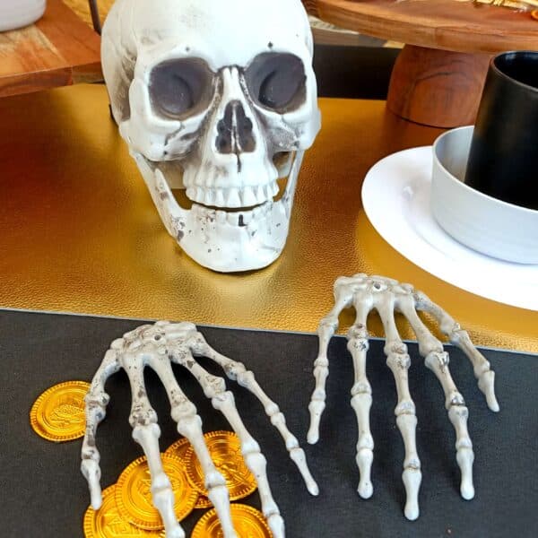 A pirate party table set up with black table cloth, skeletons, gold and plates