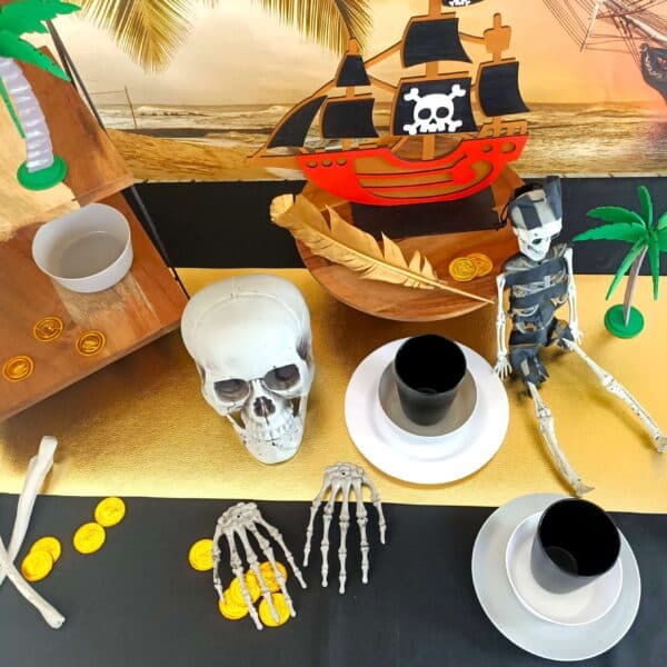 A pirate party table set up with black table cloth, skeletons, gold and plates