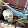 A wooden treasure chest sits open. There is a net, skull, swords and treasure inside. There is a treasure map in front of it.